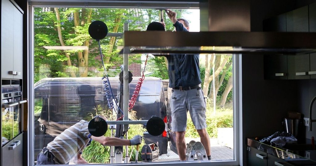 Deux poseurs installant une grande baie vitrée au palonnier à ventouses à Château-Gontier par Kalio Menuiserie