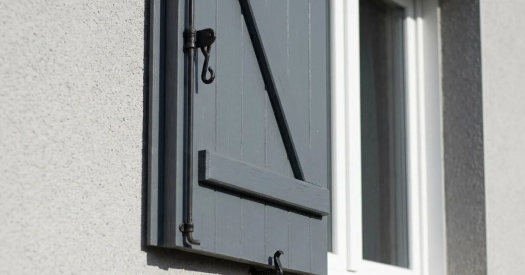Volet battant en bois entrouvert devant une fenêtre PVC fermée